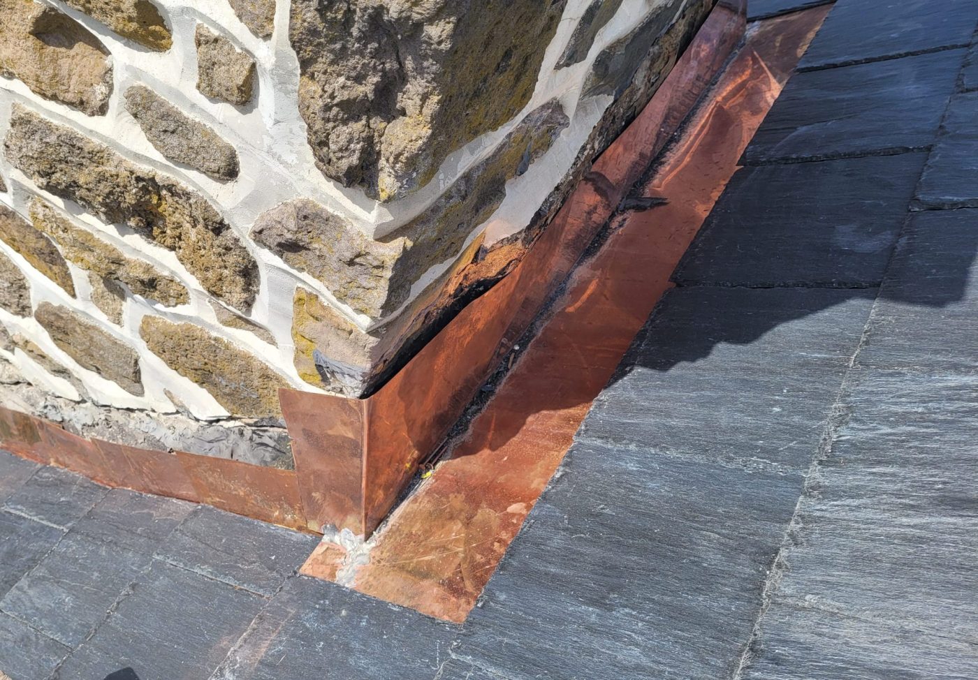 Close-up of newly installed copper flashing on a historic brick chimney and slate roof, crafted by Behan Construction.